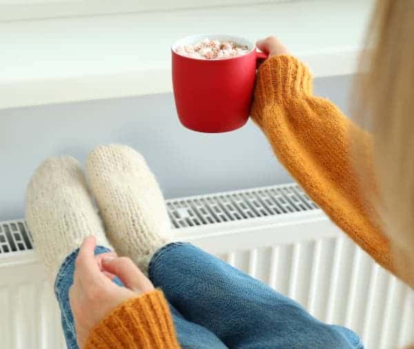 feet up on a radiator holding a mug of hot chocolate